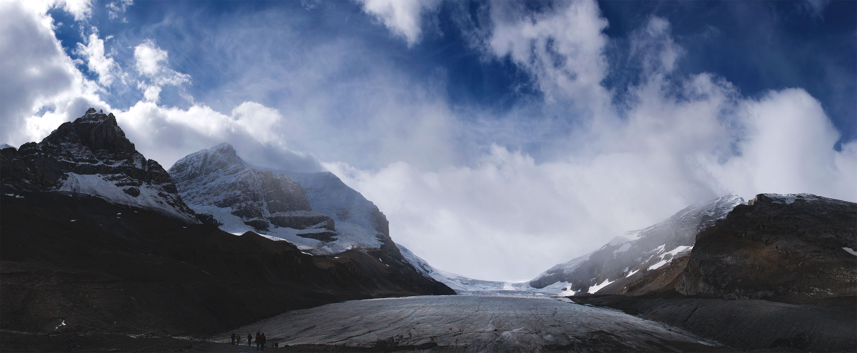 A panoramic photo of the Athabasca Glacier, two big mountains and in the middle the glacier. The walk to this glacier has markers showing how far down the glacier used to reach